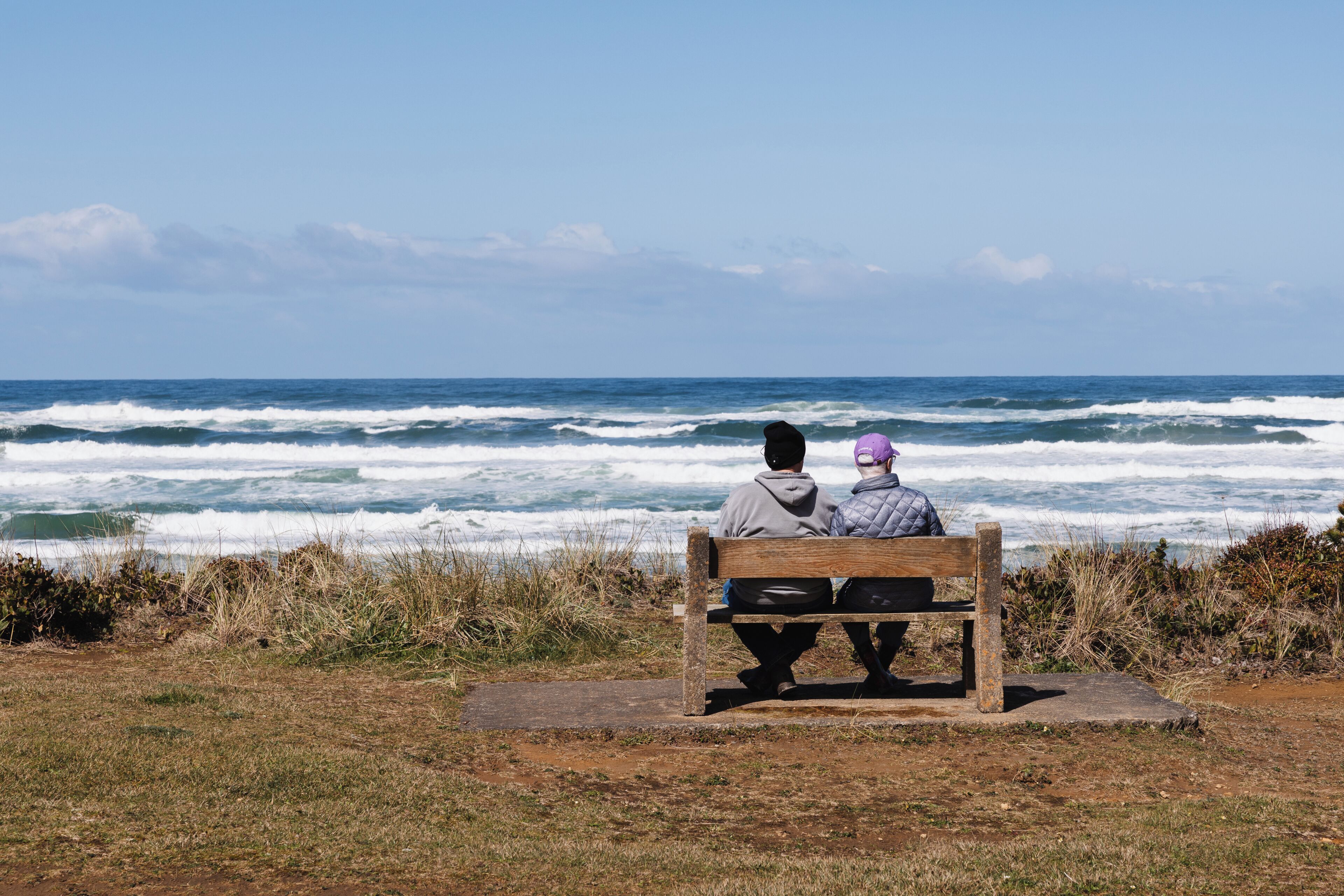Deux personnes sont assises sur un banc, face à l’océan.