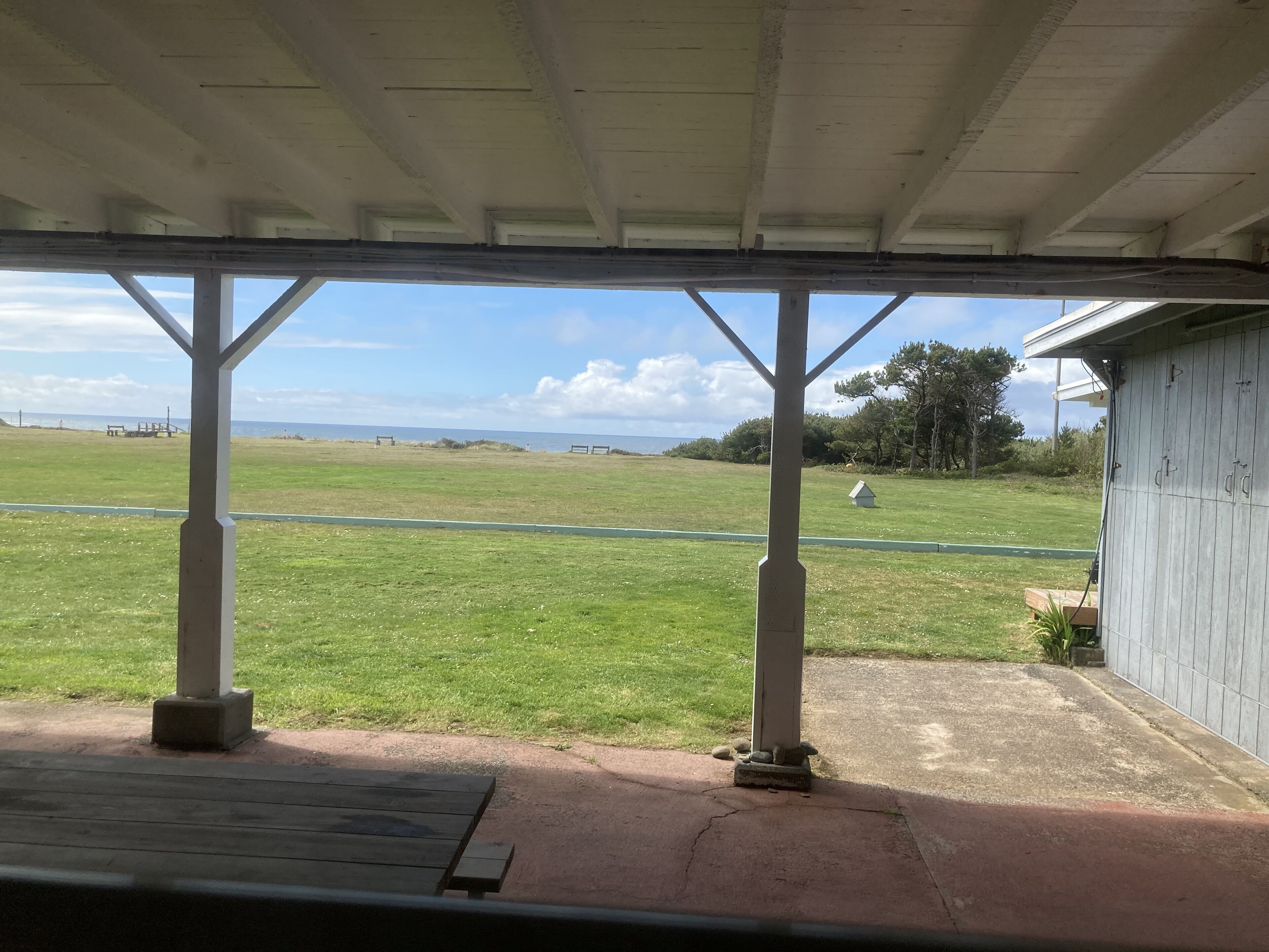 Un espacio al aire libre techado con vistas a un campo verde y un edificio pequeño a lo lejos.