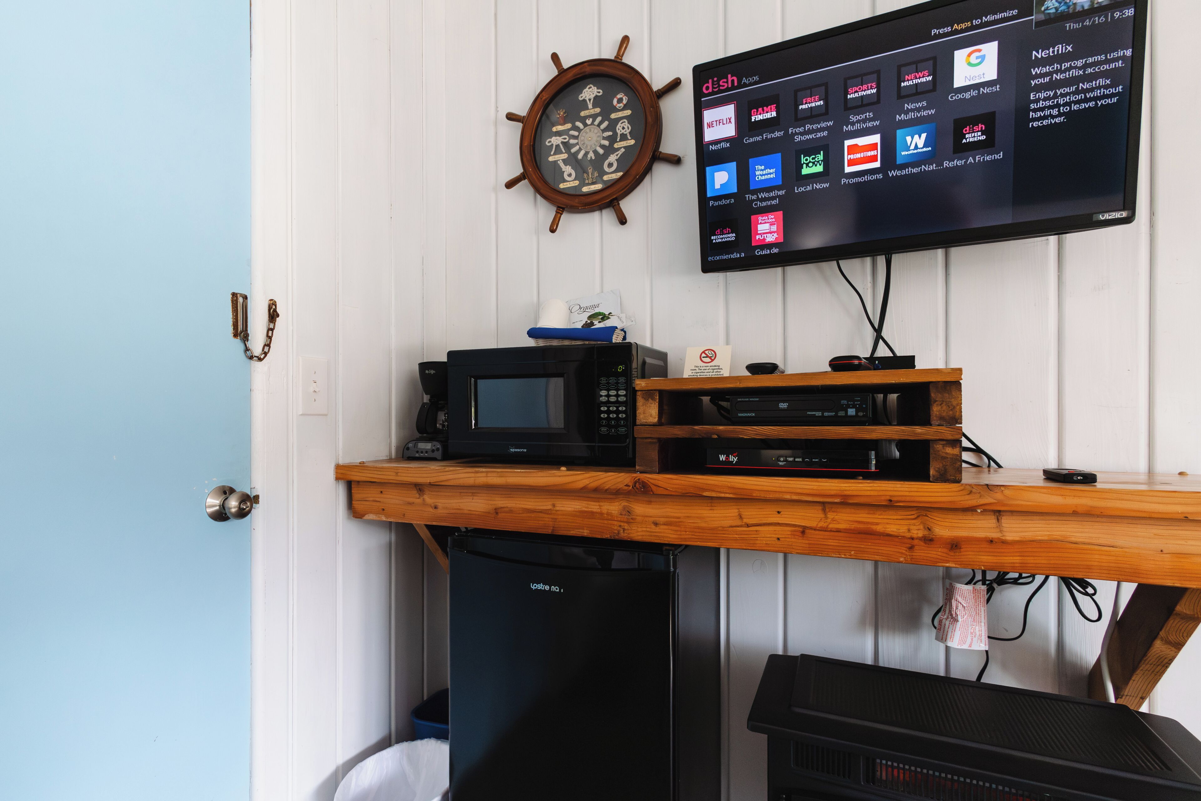 Une pièce comprenant un bureau en bois, un four à micro-ondes, un téléviseur affichant diverses applications et une horloge murale.