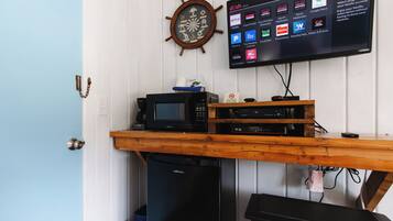 Une pièce comprenant un bureau en bois, un four à micro-ondes, un téléviseur affichant diverses applications et une horloge murale.
