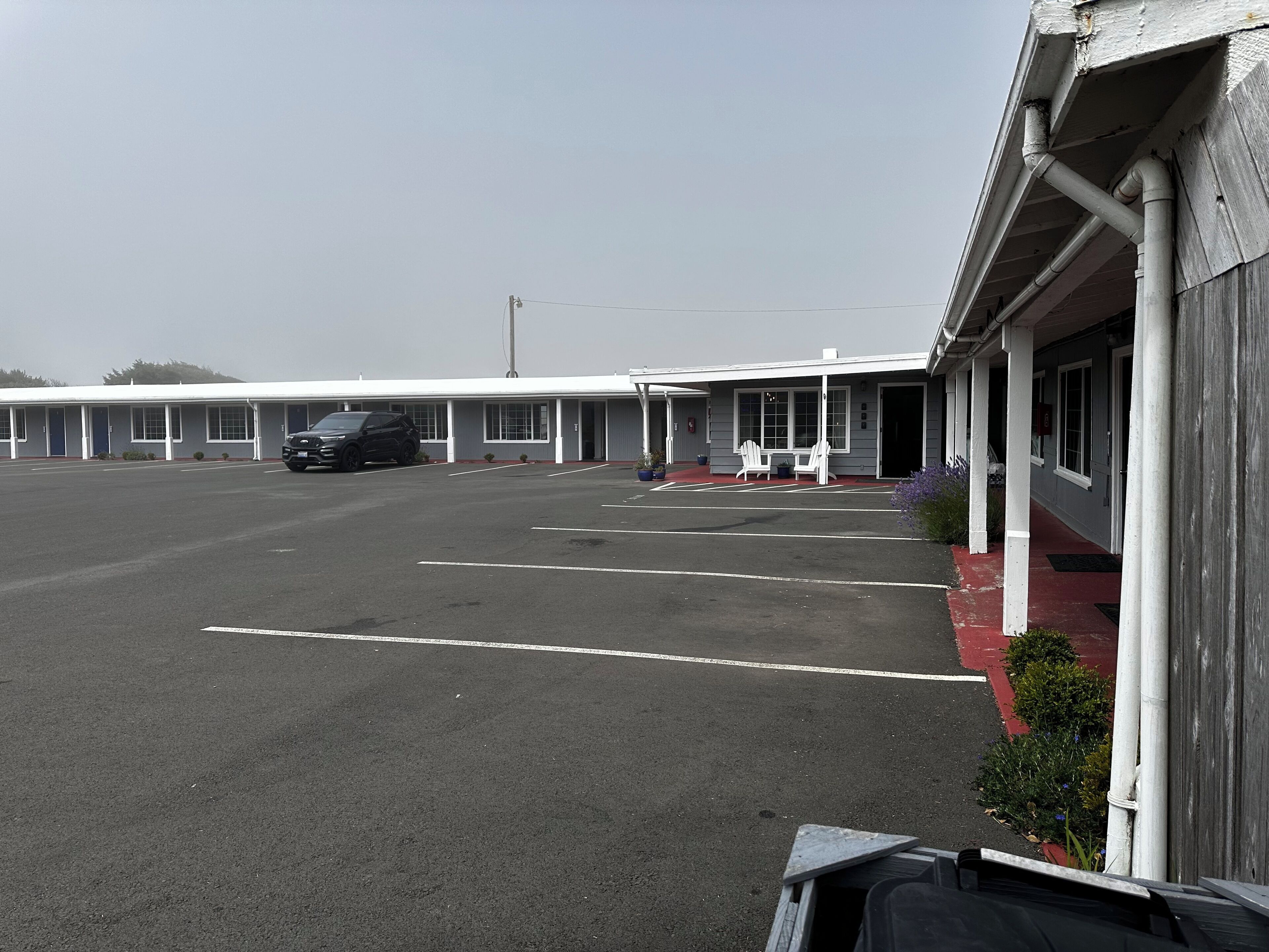 Ein Motel mit Parkplatz, einer Reihe von Zimmern und einer überdachten Außenbereich-Sitzgelegenheit.