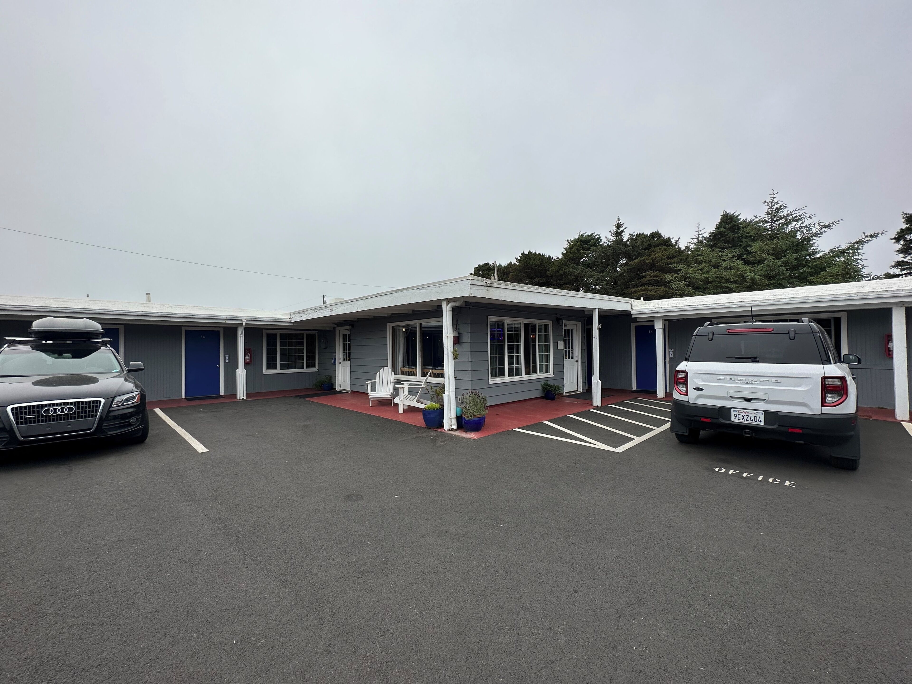 A motel with two parking spaces, a covered porch, and a small outdoor seating area.
