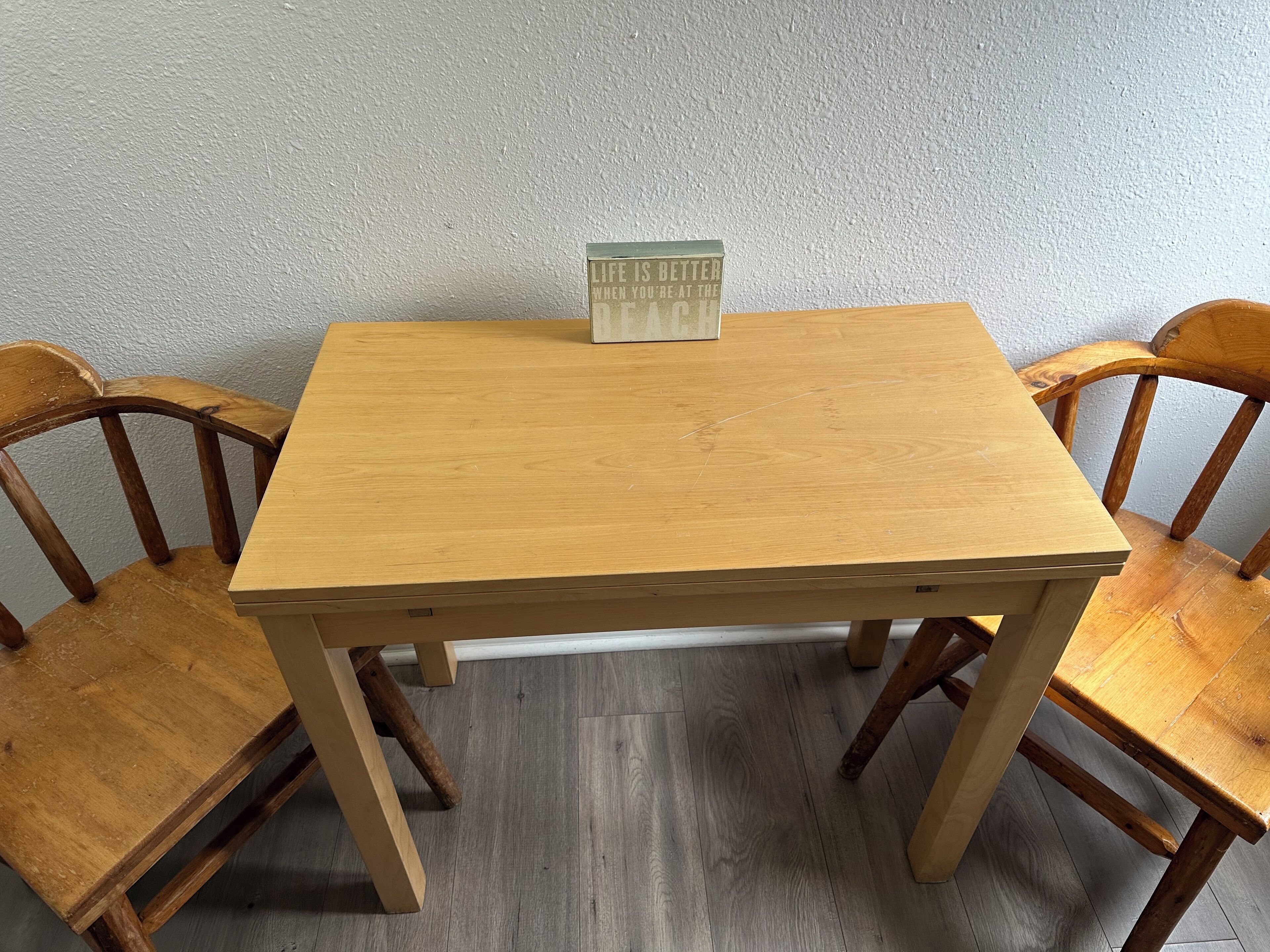 A wooden table with a small sign on top, surrounded by four wooden chairs.