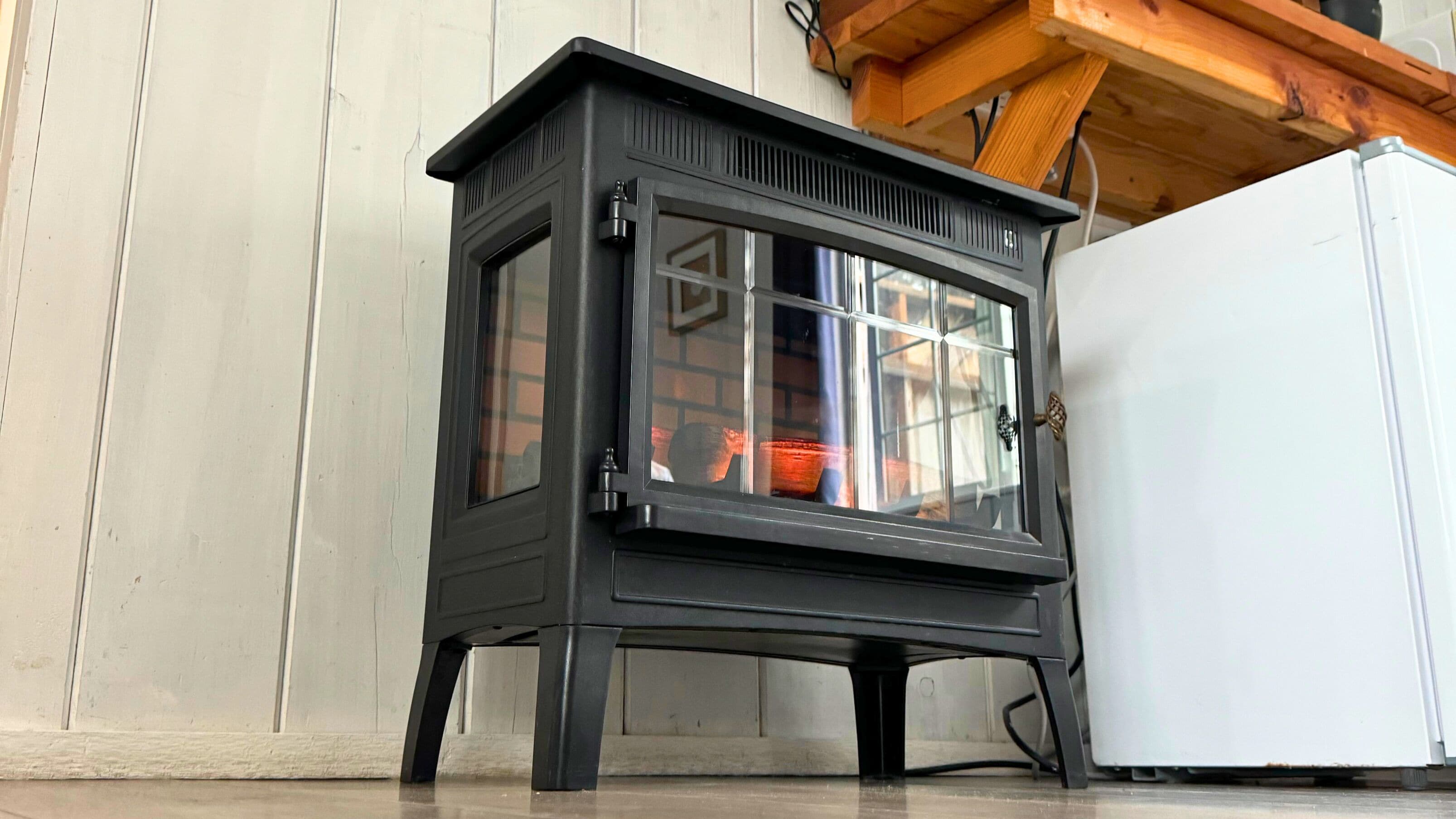 A black wood-burning stove with a glass door, a white refrigerator, and a wooden ceiling beam.
