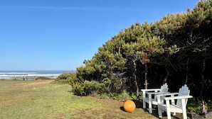 Un espacio exterior junto a la costa con bancos y sillas, una pelota naranja grande, y vistas al océano.