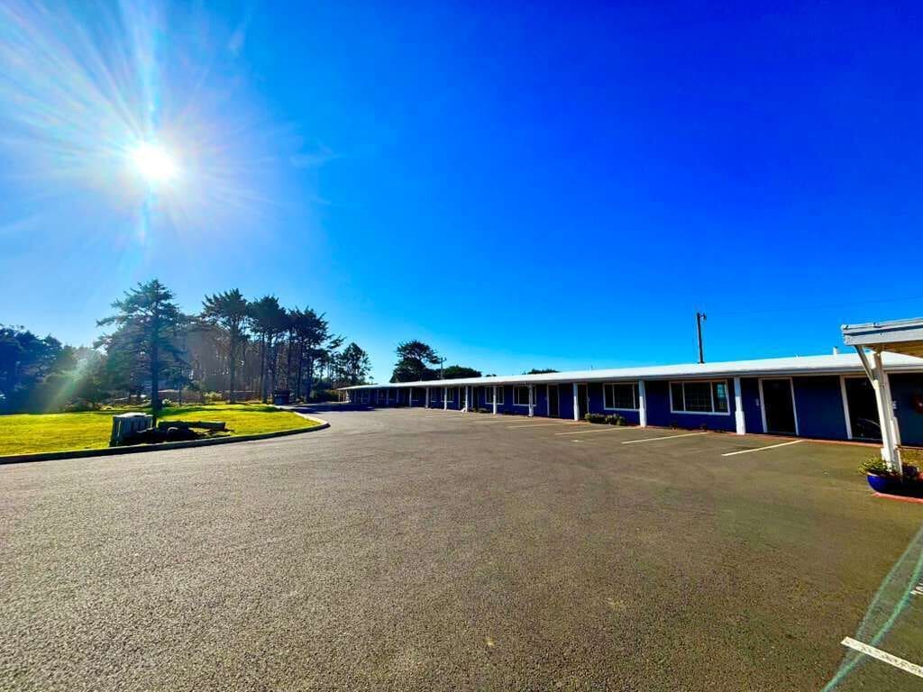 A motel with a parking lot, a row of rooms, and a clear blue sky.