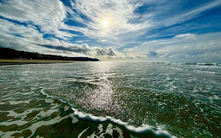 A beach with waves, a clear sky, and a sun.