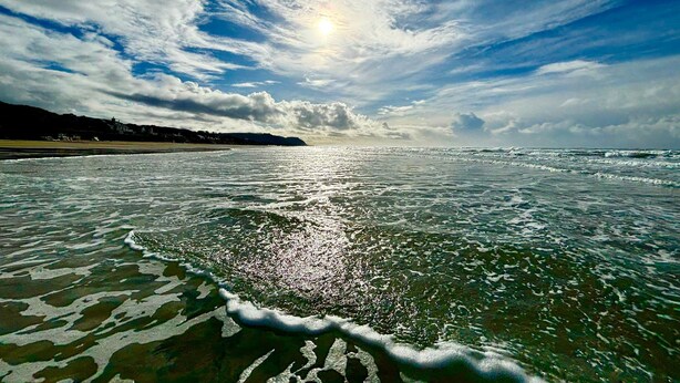 Una playa con olas, cielo despejado y sol.