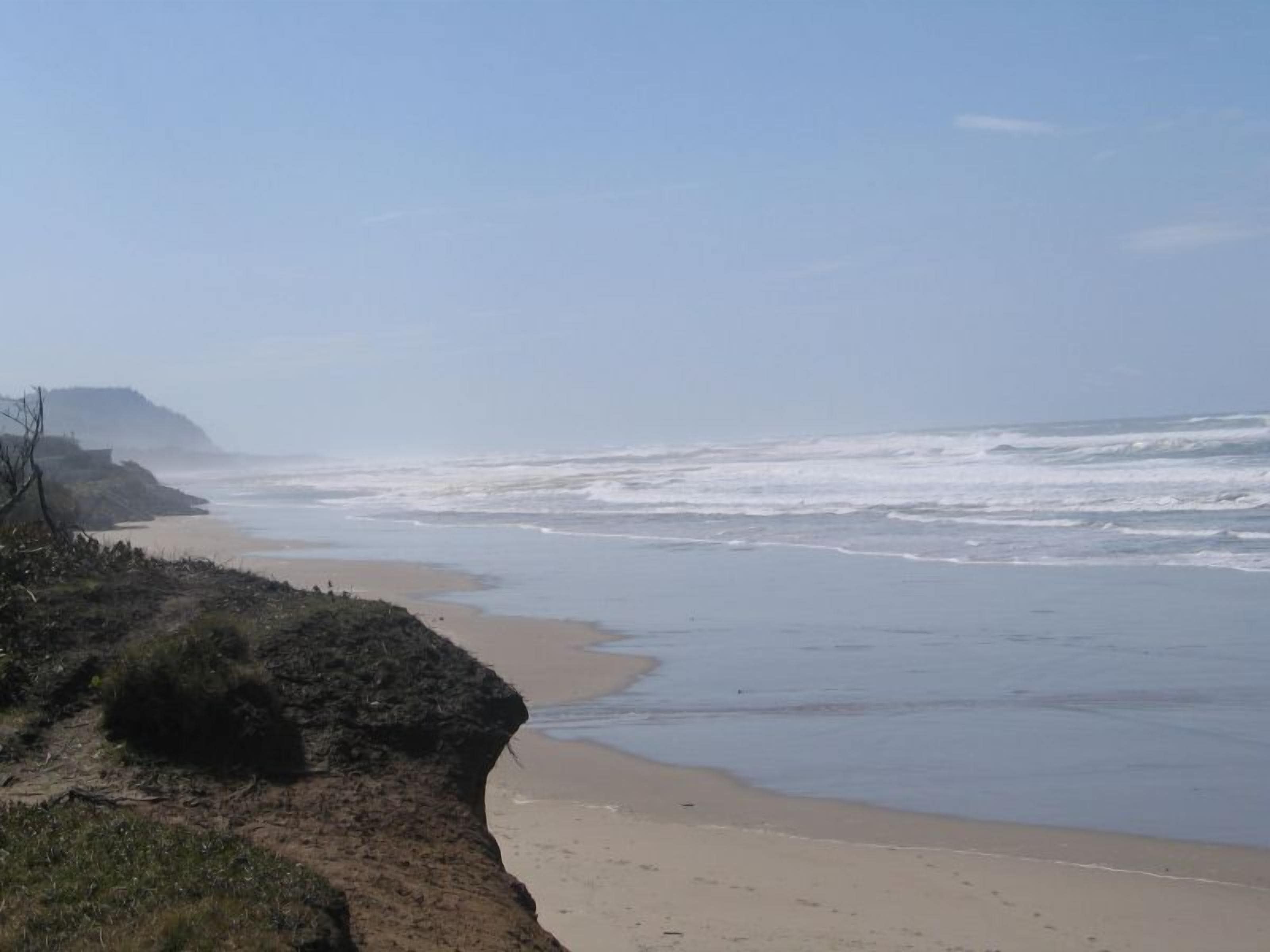 Una playa con olas, una orilla de arena y un acantilado.