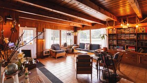 Interior acogedor de una cabaña con paredes de madera, una chimenea, un sofá, una mesa de comedor y una estantería llena de libros.
