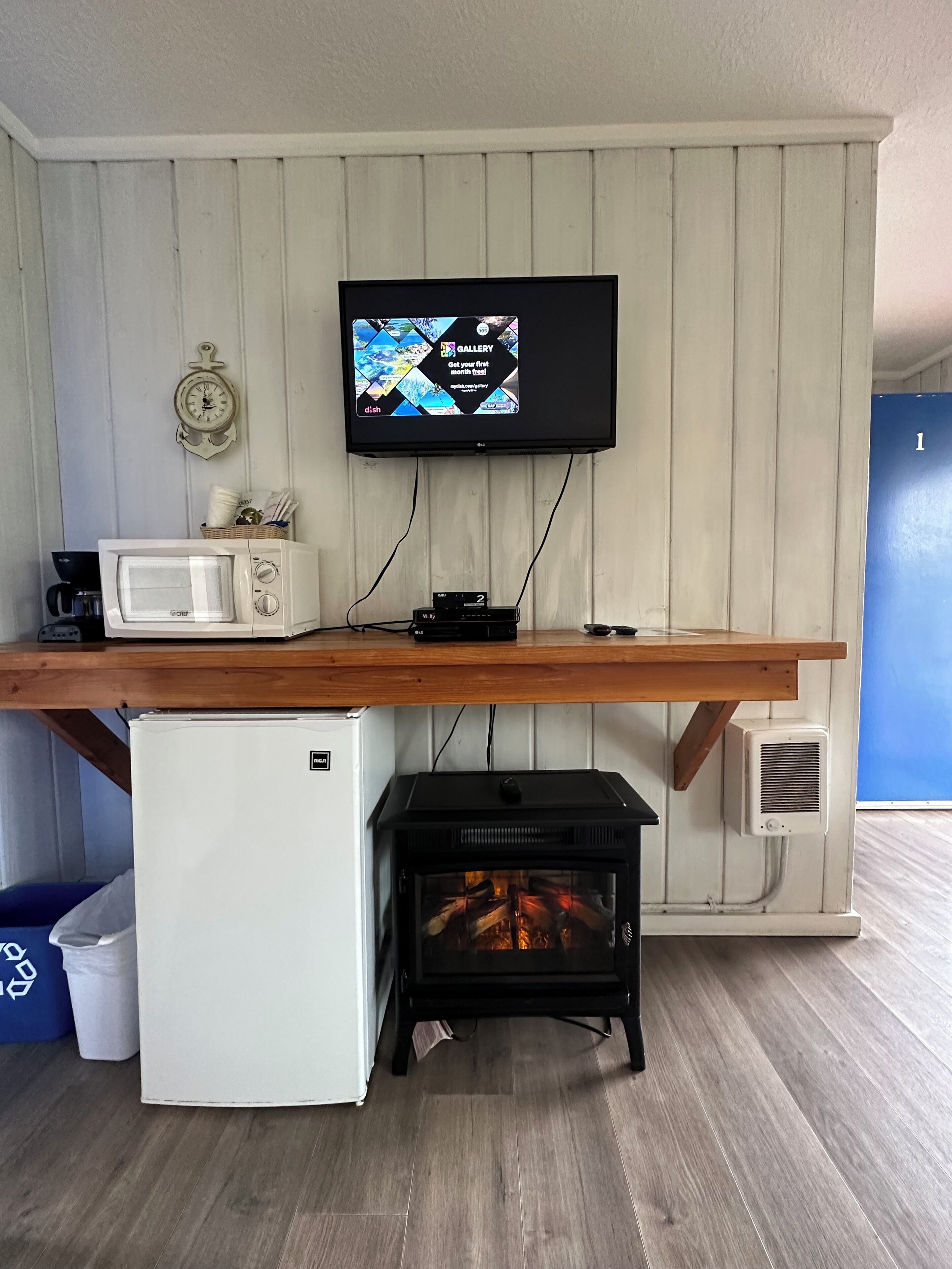 Cocina compacta con microondas, un refrigerador pequeño, estufa de leña y televisor montado en la pared.