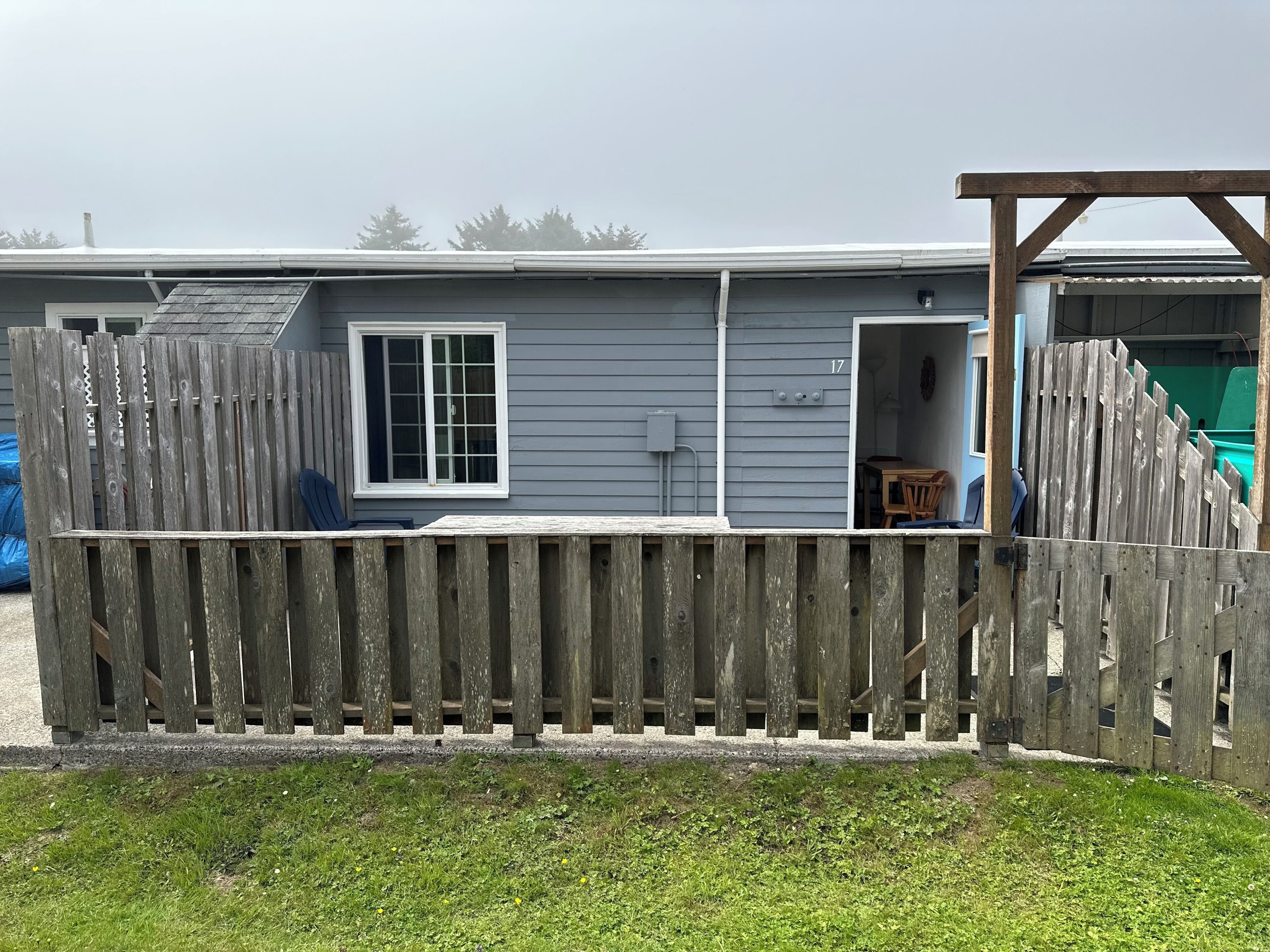 A single-story house with a grey exterior, a white window, and a wooden deck.