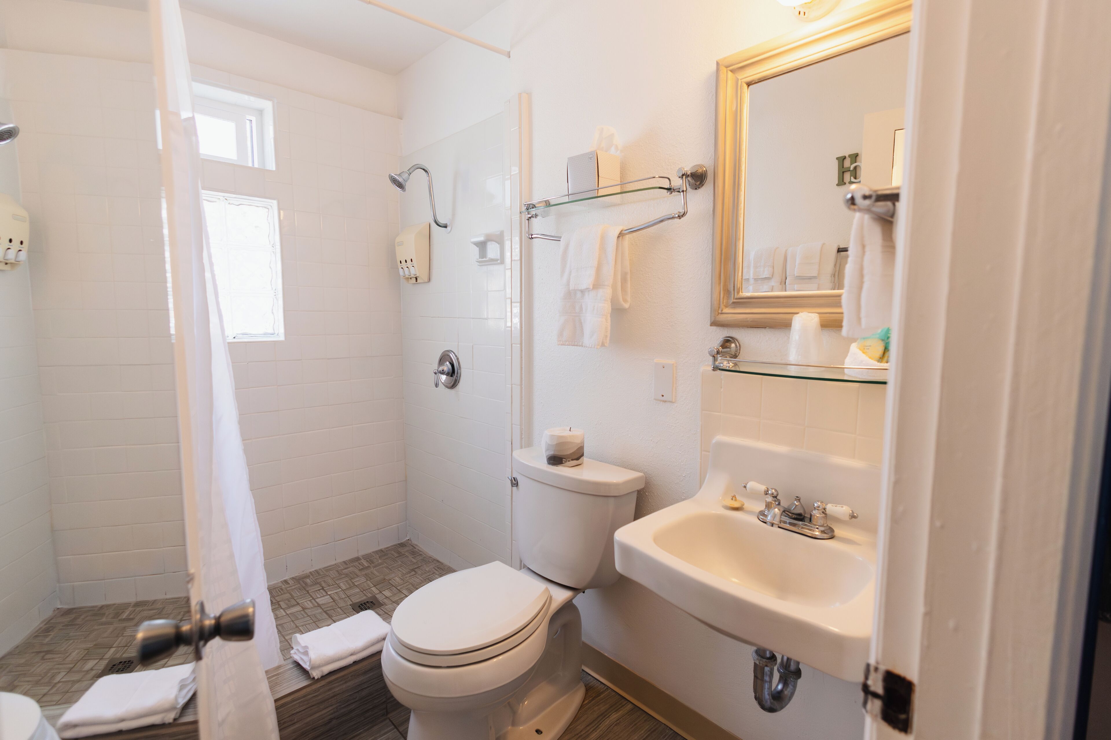 A bathroom with a shower, toilet, sink, and a mirror.