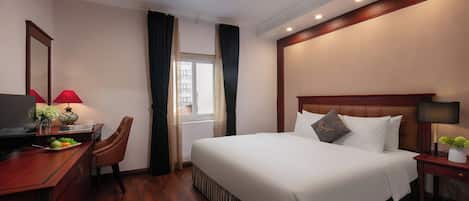 A hotel room with a large bed, a desk with a computer, a chair, and a window with curtains.
