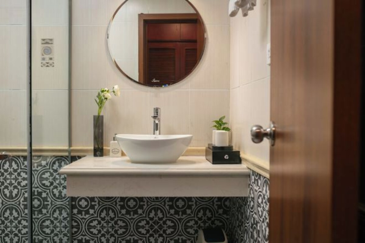 Casa de banho com um espelho redondo, uma sanita branca e azulejos estampados.