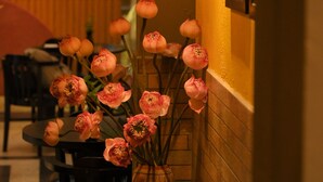 Rincón de un restaurante con una mesa, sillas, un florero y un televisor montado en la pared.