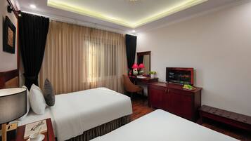A hotel room with two beds, a desk, a TV, and a bench.