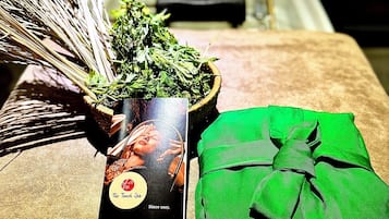 Una cesta de mimbre llena de hierbas verdes, un paño verde atado con un lazo y una tarjeta negra con el logotipo y texto de un spa.