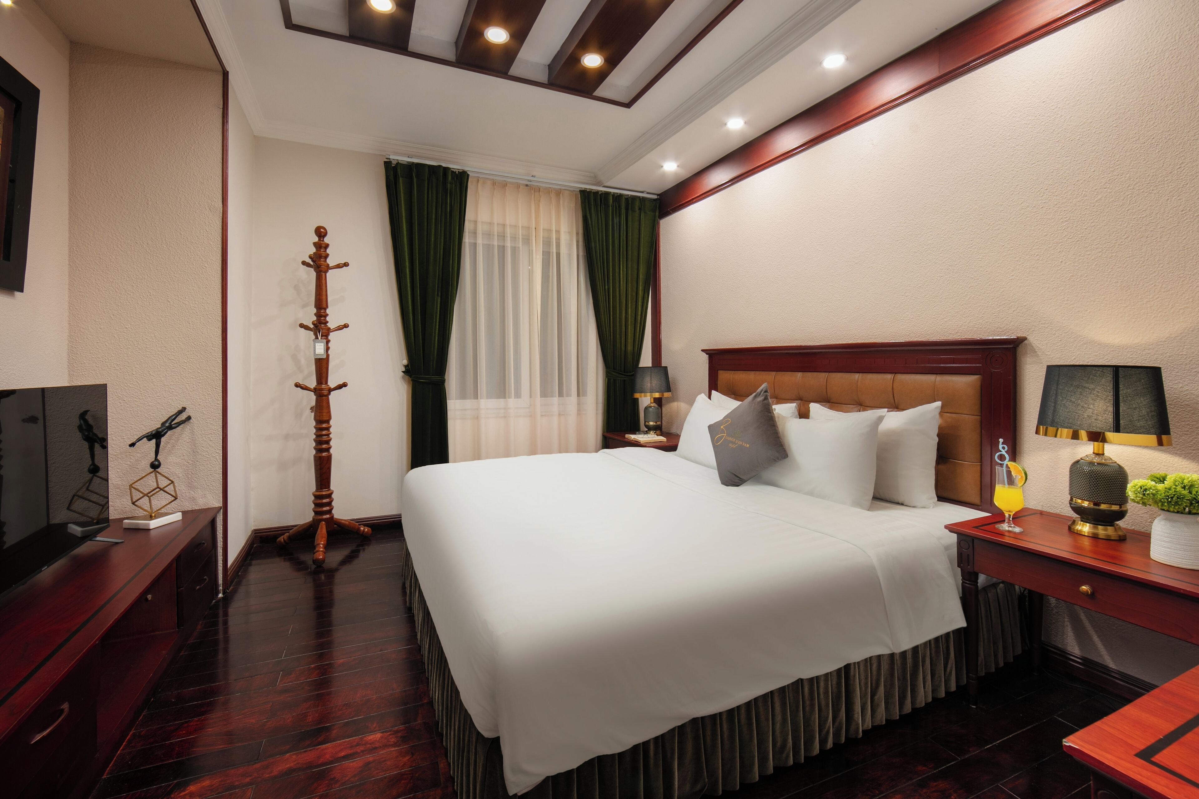 A hotel room with a large bed, a wooden side table, a TV, and a coat stand.
