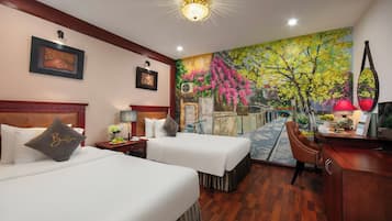 A hotel room with two beds, a desk, a chair, and a mural of a tree with pink flowers.