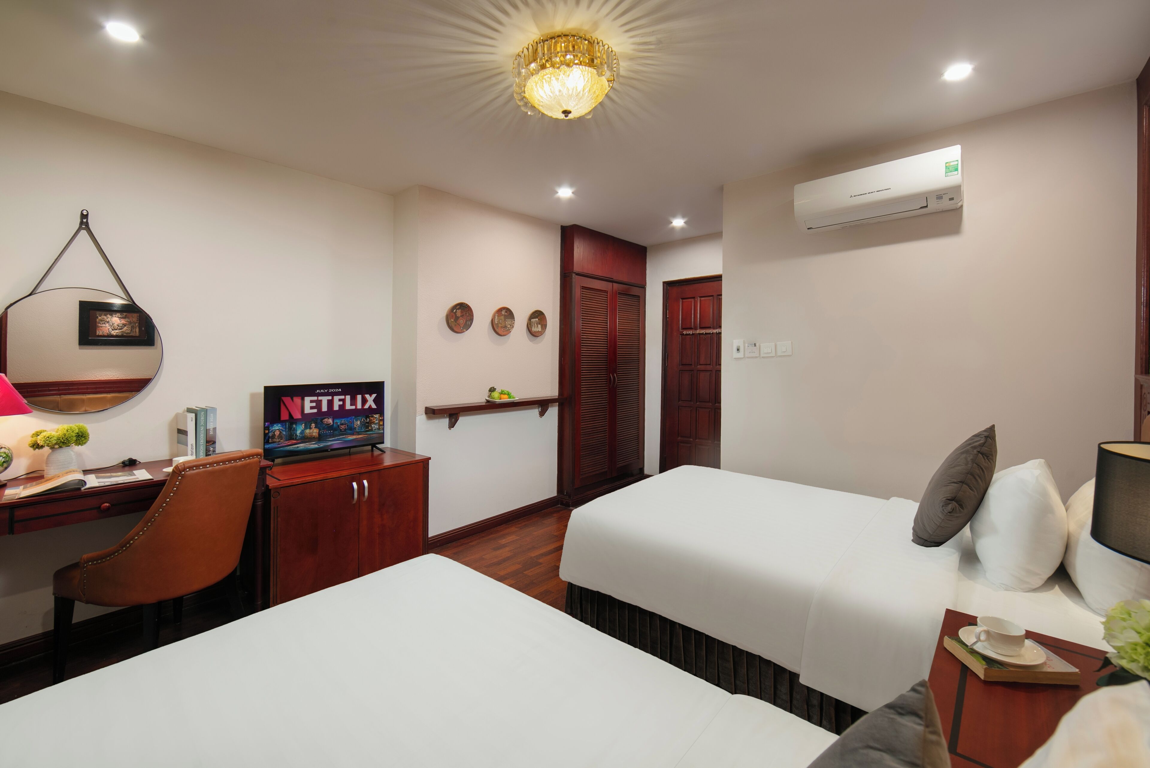 Habitación de hotel con dos camas, un escritorio con silla, televisión y aire acondicionado instalado en la pared.