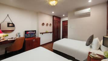 Habitación de hotel con dos camas, un escritorio con silla, televisión y aire acondicionado instalado en la pared.