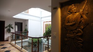Un interior moderno con barandilla de vidrio, una estatua y vista a un patio.