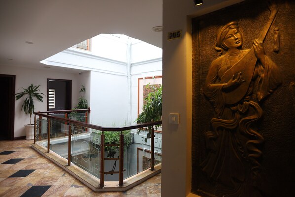 A modern interior with a glass railing, a statue, and a view of a courtyard. - Bonjour D'An Nam Home (Hanoi)
