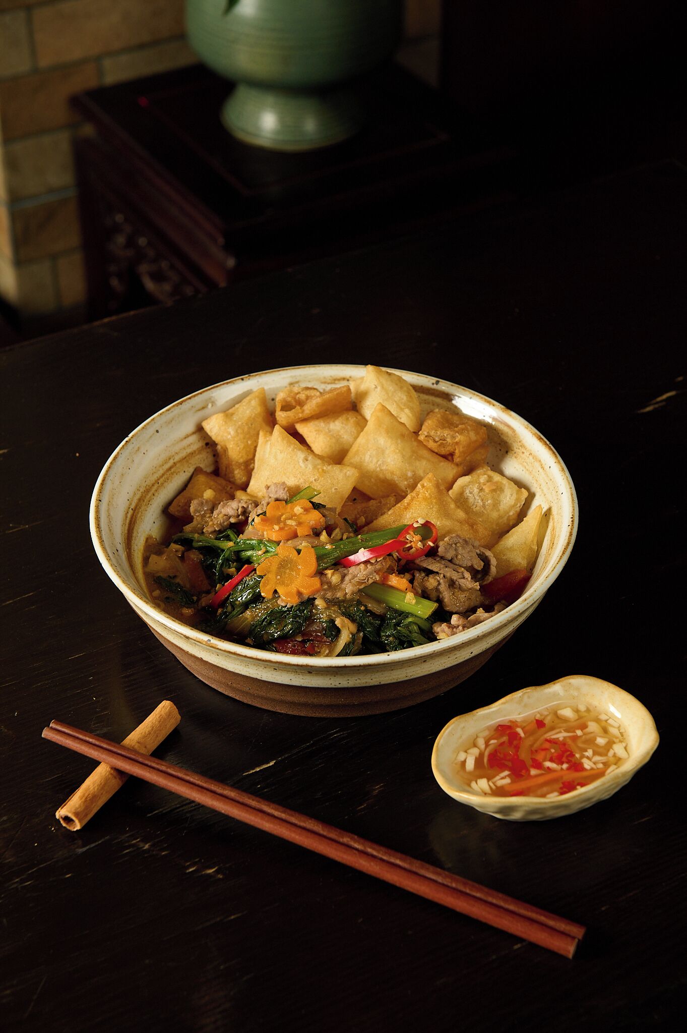 A bowl of food with chopsticks and a small bowl of sauce on a table.