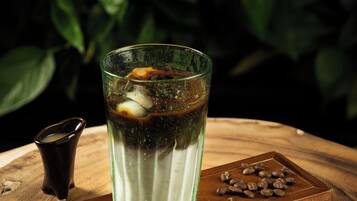 Een glas ijskoud drankje op een houten tafel, met losse koffiebonen en een klein kopje.