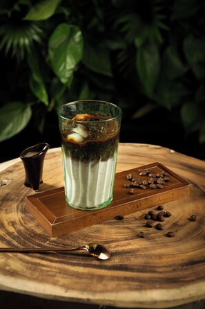 A glass of iced beverage on a wooden table with scattered coffee beans and a small cup. - Bonjour D'An Nam Home (Hanoi)