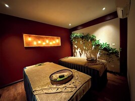 A room with two beds, a wall-mounted light fixture, a potted plant, and a wall-mounted air conditioner.