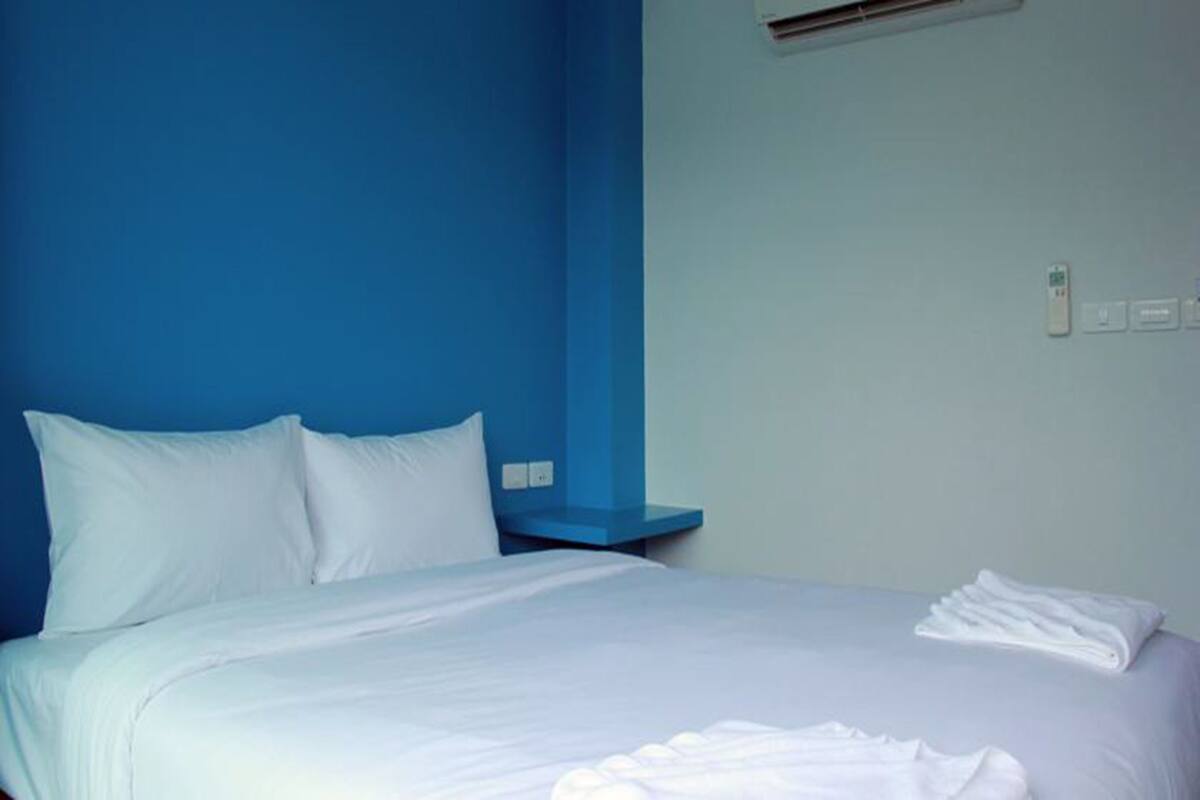 A hotel room with a bed, white bedding, a blue accent wall, and a wall-mounted control panel.
