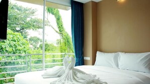 A hotel room with a large bed, a view of greenery through a window, and a blue curtain. - Cheeky Monkey's Samui (Koh Samui)