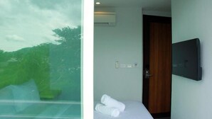 A hotel room with a bed, a TV mounted on the wall, and a window with a view of trees. - Cheeky Monkey's Samui (Koh Samui)