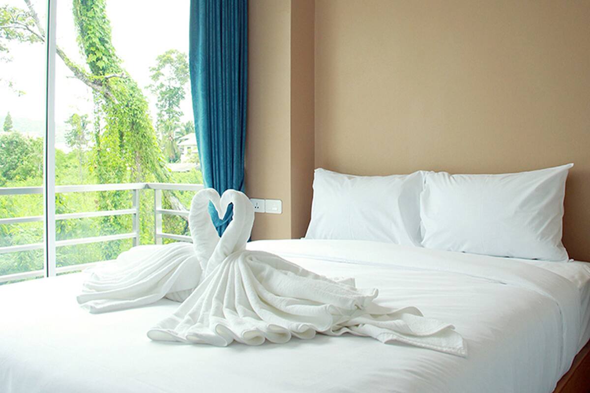 A hotel room with a bed, white pillows, and a blue curtain.