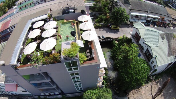 A rooftop pool with umbrellas, surrounded by greenery and buildings. - Cheeky Monkey's Samui (Koh Samui)