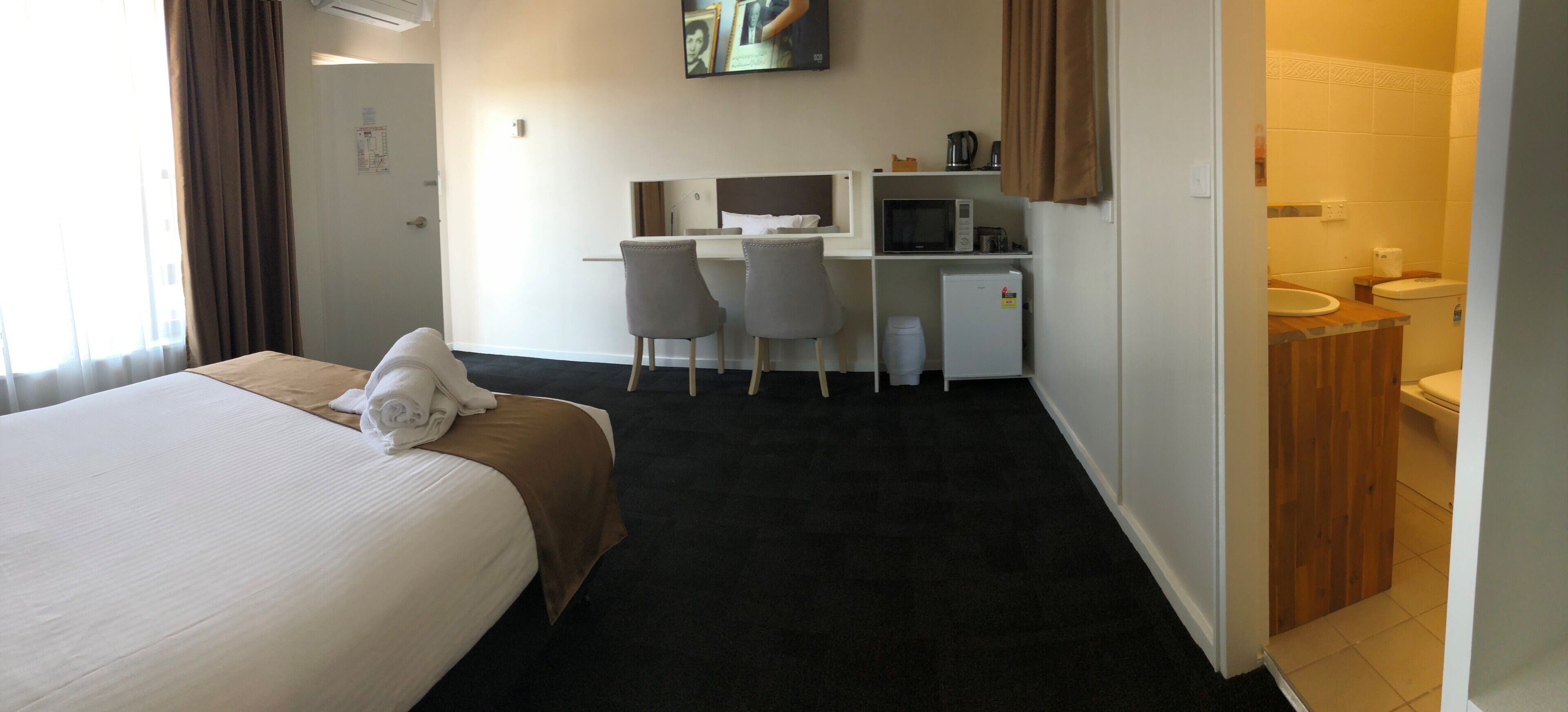 A hotel room with a bed, two chairs, a desk with a computer, a microwave, and a small refrigerator.