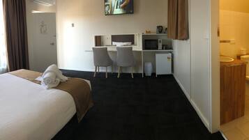 Ein Hotelzimmer mit einem Bett, zwei Stühlen, einem Schreibtisch mit Computer, einer Mikrowelle und einem kleinen Kühlschrank.