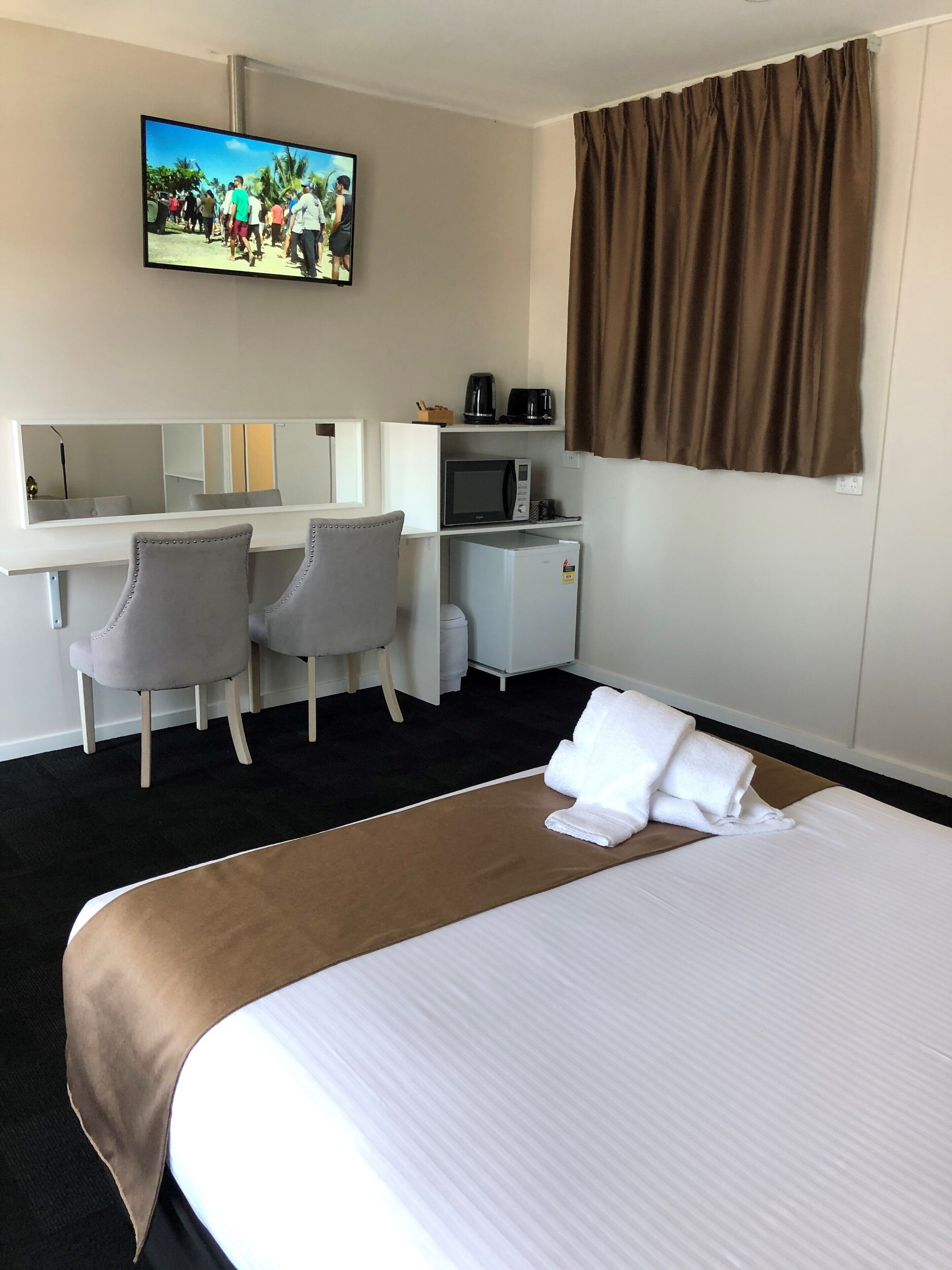 A hotel room with a bed, a desk with two chairs, a microwave, a coffee maker, and a television on the wall.