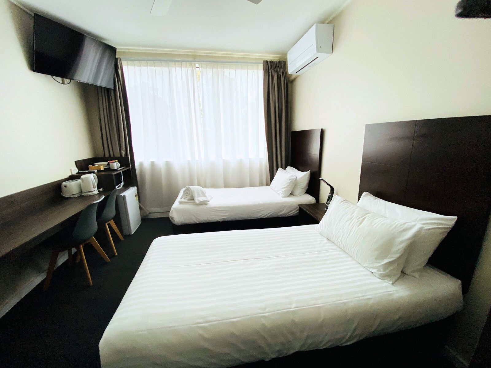 A hotel room with a large bed, a desk with a chair, a TV mounted on the wall, and an air conditioning unit.