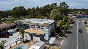 A motel with a signboard, a swimming pool, and a road with cars.