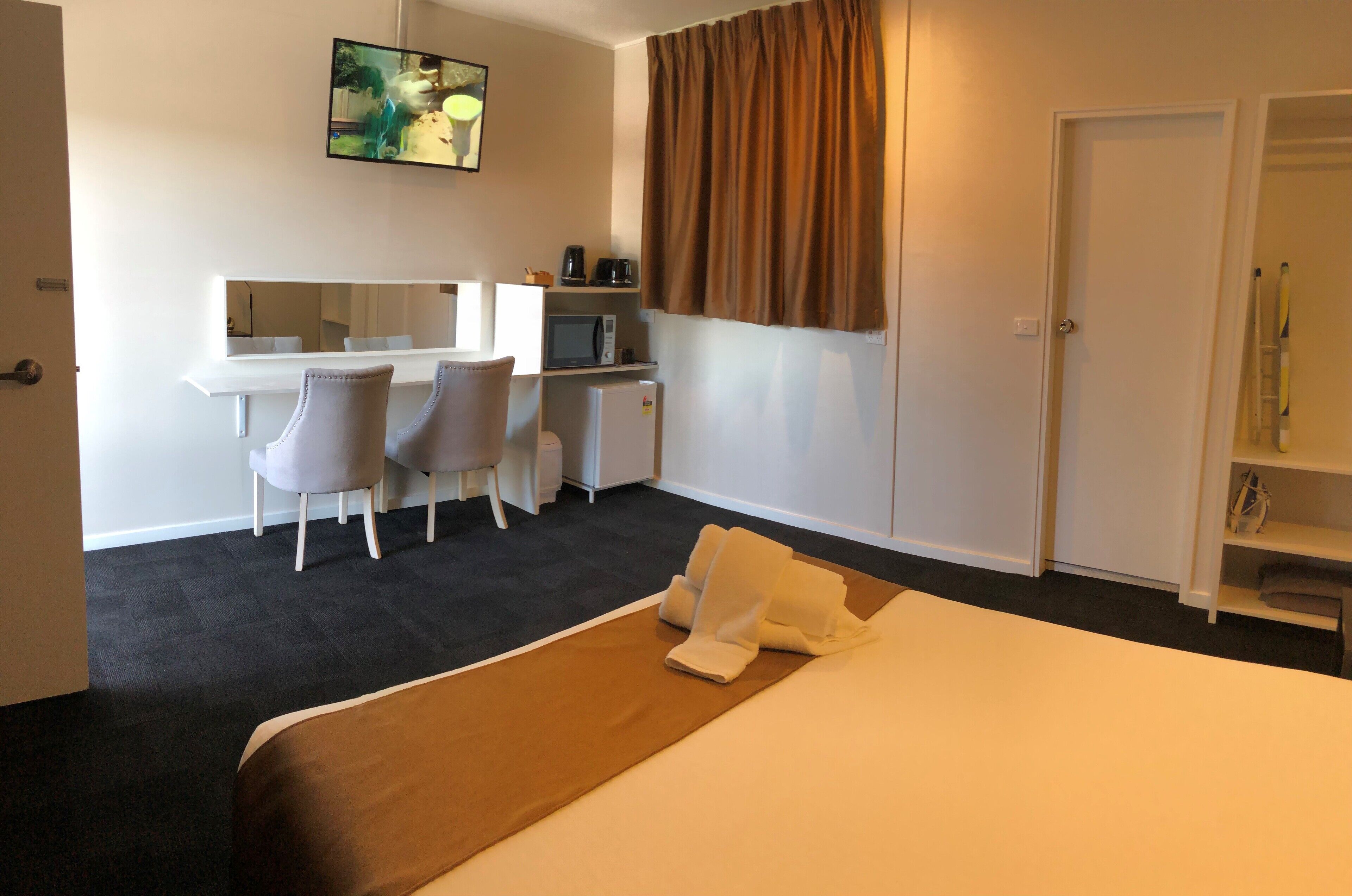 Habitación de hotel con cama, escritorio con silla, microondas y televisión en la pared.
