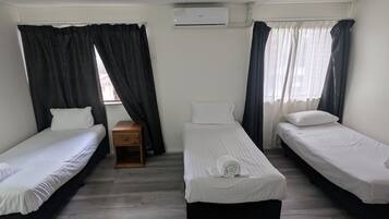 A room with three single beds, a wooden nightstand, and a window with curtains.