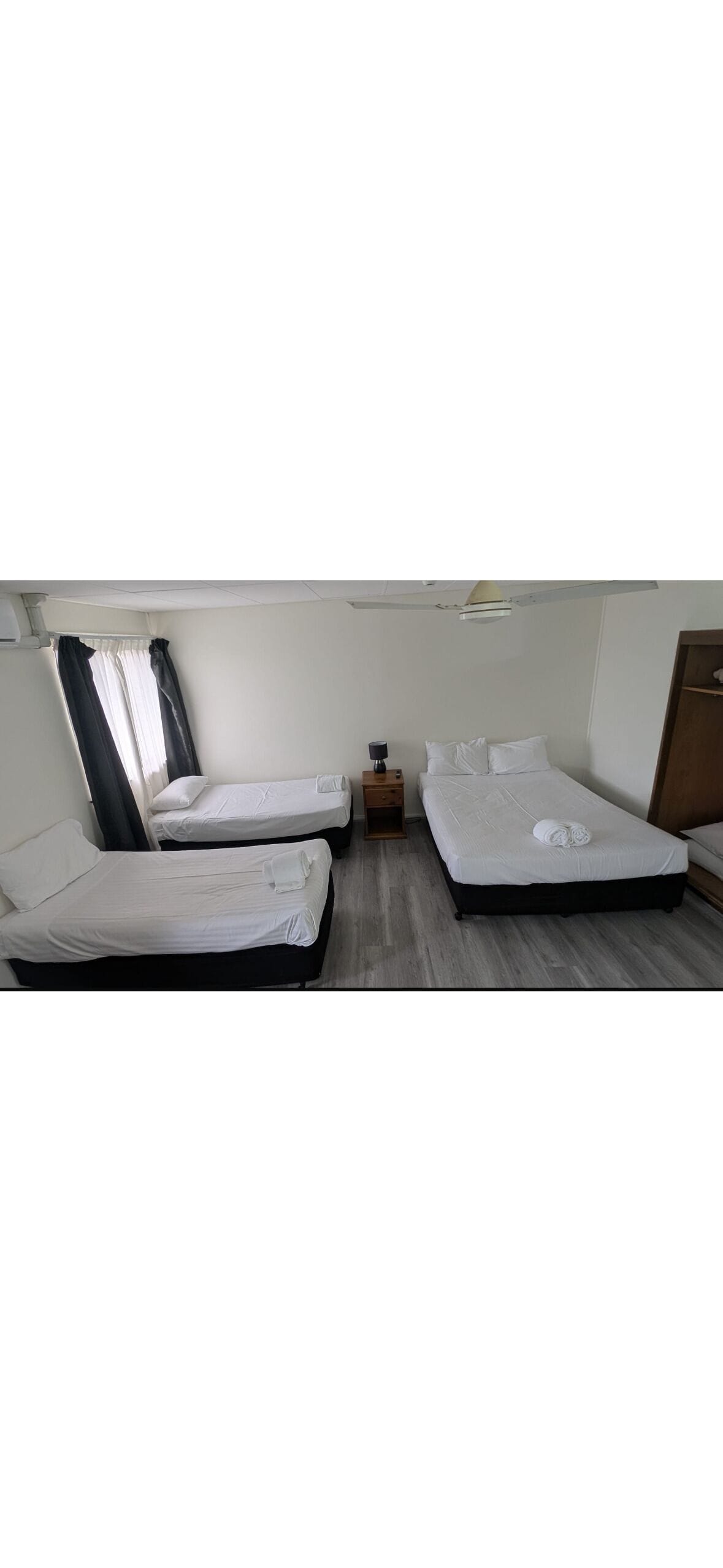 A room with two single beds, a small bedside table, a lamp, and a wardrobe.