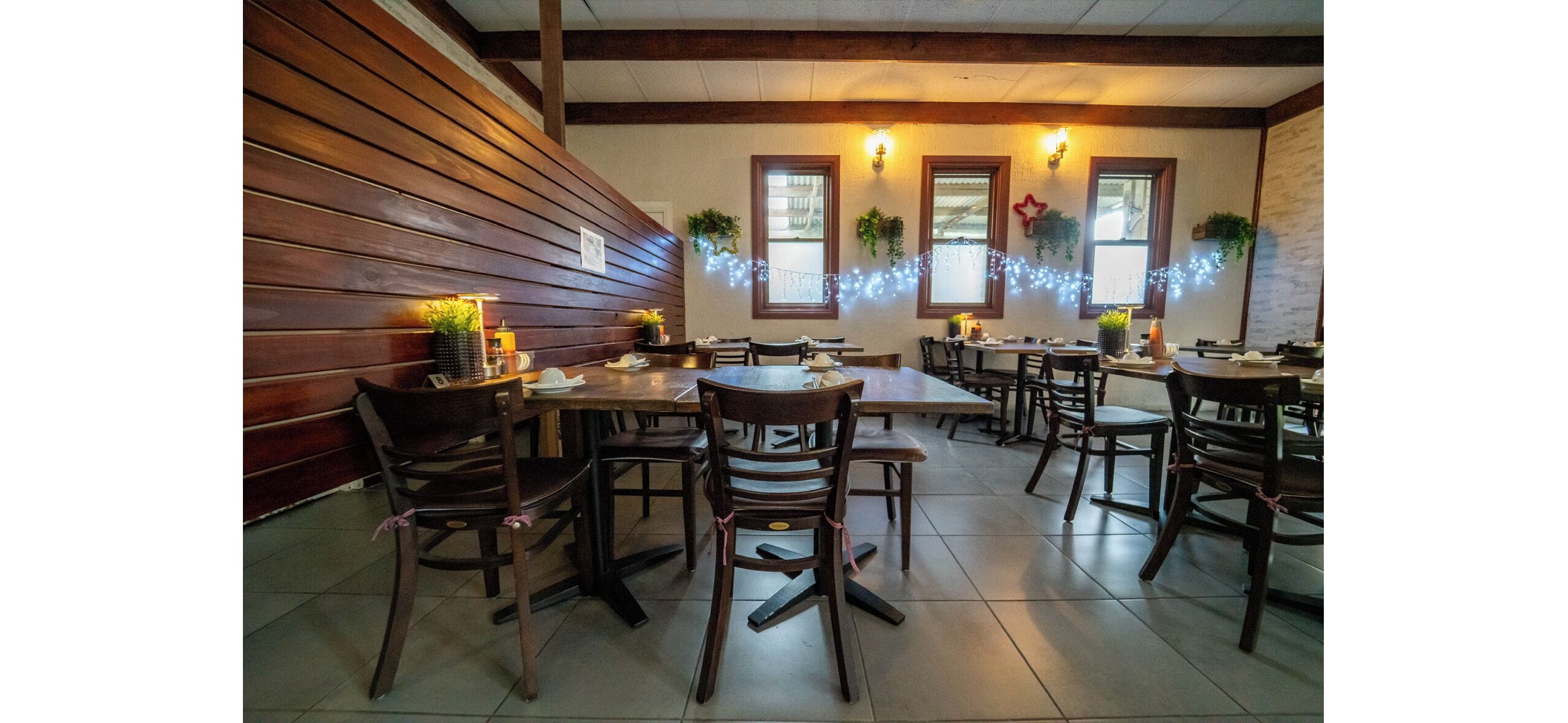 A restaurant with wooden walls, multiple tables and chairs, and string lights.