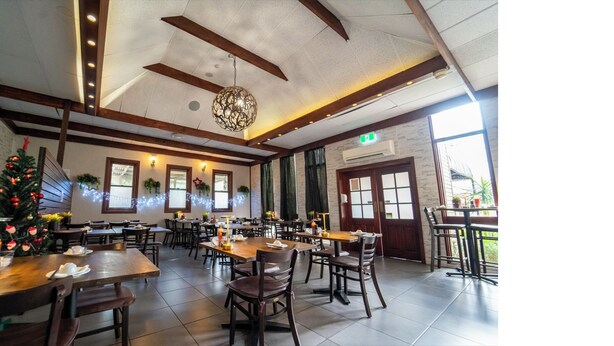 A spacious dining area with wooden tables and chairs, a Christmas tree, and large windows allowing natural light.
