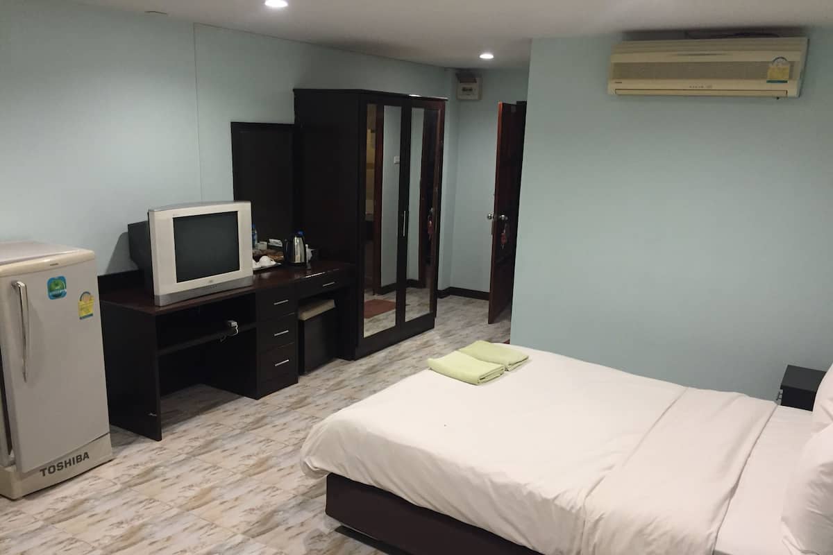 Un dormitorio con cama, televisor sobre un mueble, armario y refrigerador.
