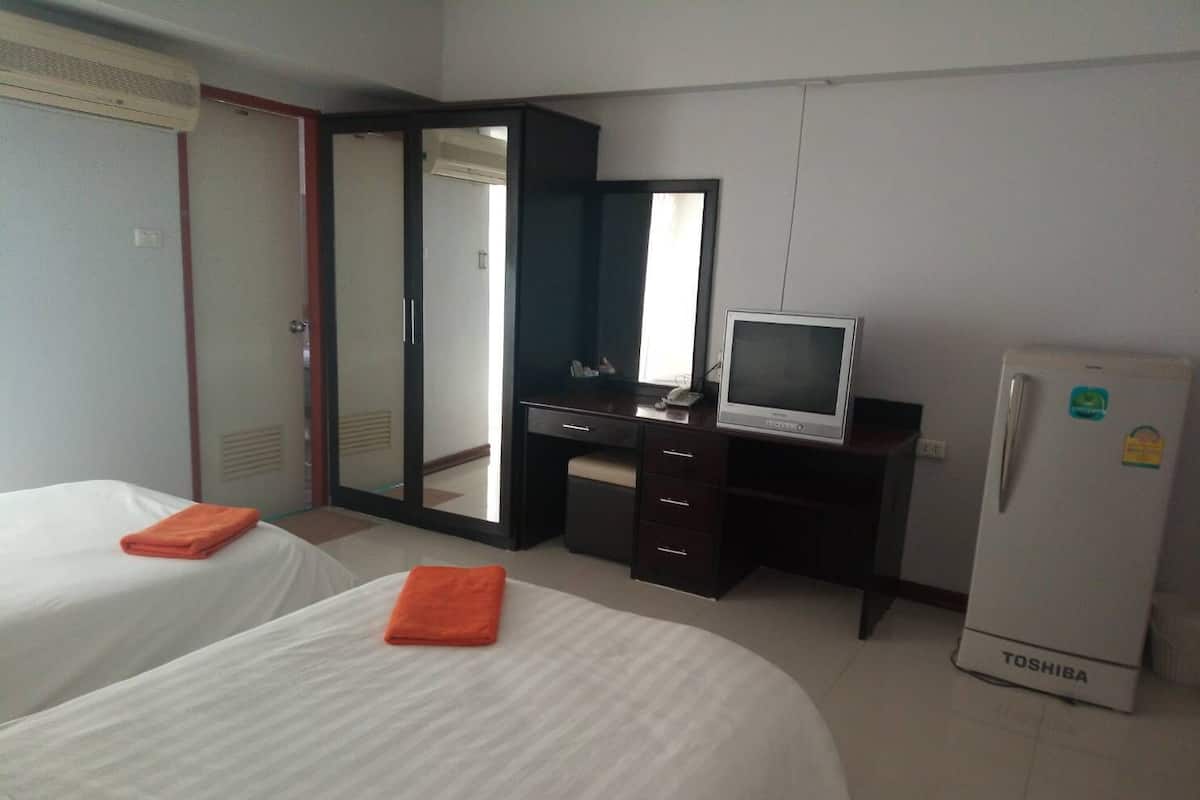 Una habitación de hotel con dos camas, un escritorio, televisor, refrigerador y un espejo grande.