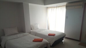 A hotel room with two beds, a window with curtains, an air conditioning unit, and a door. - Tamarind Residences (Khon Kaen)